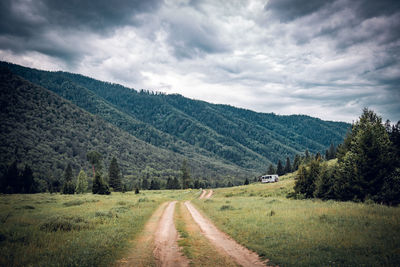 Dirt road amidst landscape and mountains against sky, altai, russia