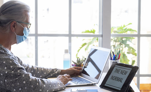 Senior woman wearing mask using laptop at home