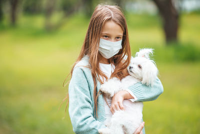 Cute girl wearing mask holding dog outdoors