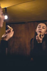 Reflection of young woman applying lipstick