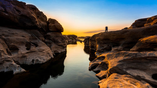 Rock formations by sea against sky during sunset