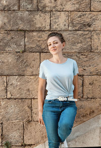 Portrait of a smiling young woman standing against brick wall