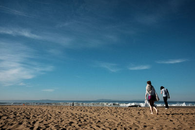 Rear view of men on beach against sky