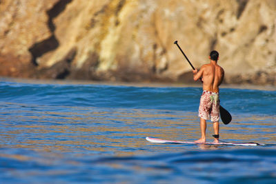 Rear view of shirtless man standing in sea