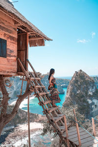 Man sitting on wood by sea against sky