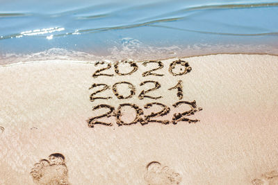 The numbers 2021, 2022 are drawn on the sand and washed away by the wave, the symbol of the new year