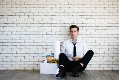 Portrait of young man sitting against wall