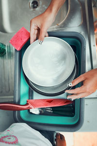 Teenager girl washing up the dishes pots and plates with help her younger sister