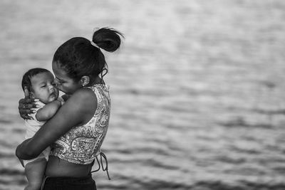 Mother kissing daughter against sea