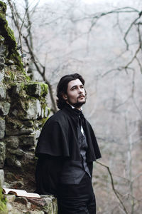 Young man in period costume standing against stone wall