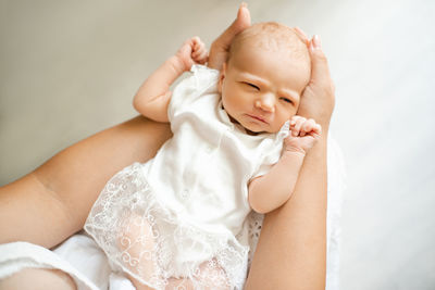 Little baby girl under 1 year old wear stylish white dress lying on mother hands in room 