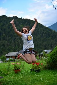 Portrait of girl jumping over field against trees