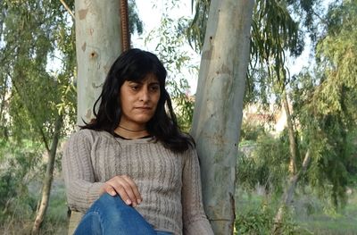 Portrait of young woman standing by tree trunk in forest