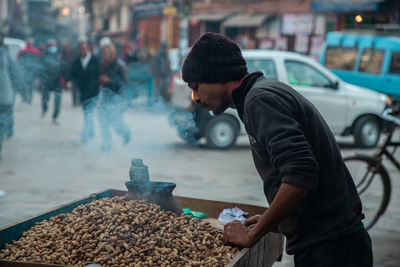 Side view of young man selling peanuts on street in city