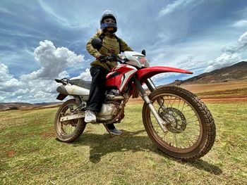 Woman with motorcycle on land against cloudy sky