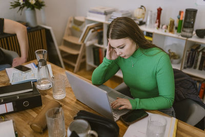 Young woman using laptop while doing school assignment at home