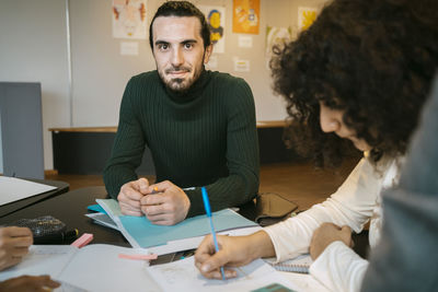 Portrait of confident young man sitting with female friend at table in university cafeteria