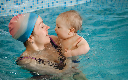 Early age swimming in pool. baby boy trained to swim in water. happy child with trainer woman in