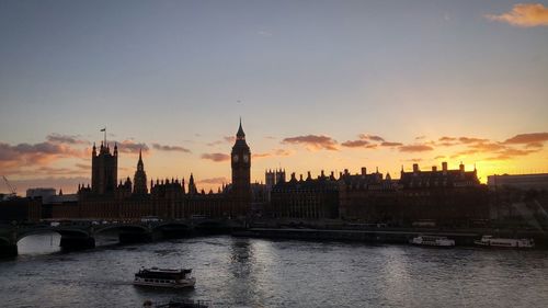 Westminster bridge over thames river by big ben against sky during sunset