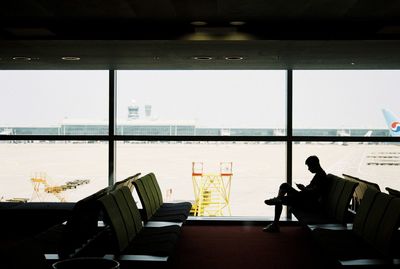 Chairs and tables at airport seen through glass window