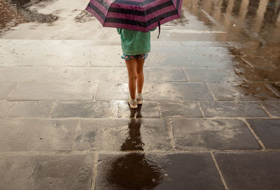 Low section of woman standing on wet footpath