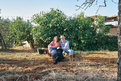 Young couple sitting on plant against trees