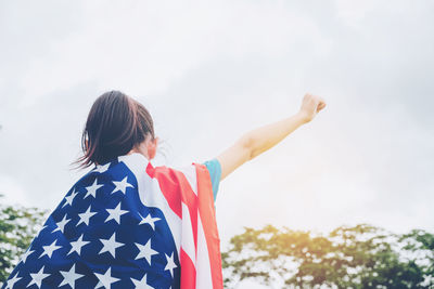 Low angle view of girl with american flag standing against sky