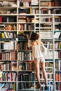 Full length rear view of woman taking books from shelves in library