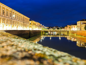 Illuminated buildings by river against sky at night