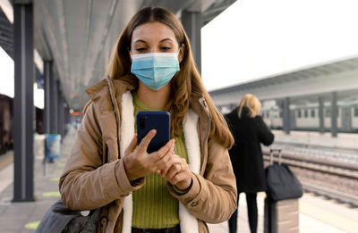 People with surgical mask using smartphone at train station