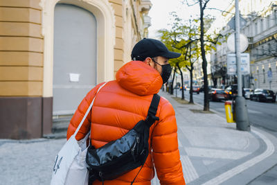 Rear view of man wearing mask walking on sidewalk