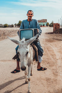 Portrait of man with television set sitting on donkey