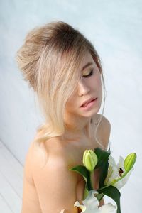 Close-up of thoughtful young woman with bouquet against wall