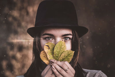 Portrait of woman wearing hat holding leaves in forest