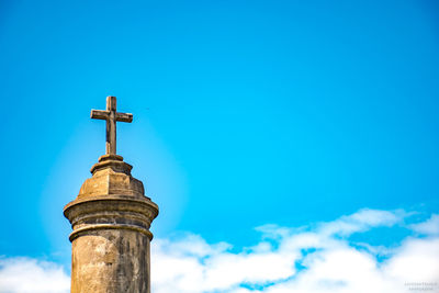 Low angle view of cross by building against blue sky