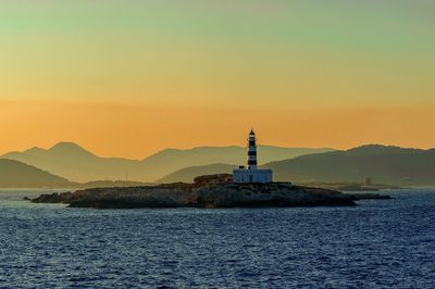 Lighthouse by sea against clear sky during sunset