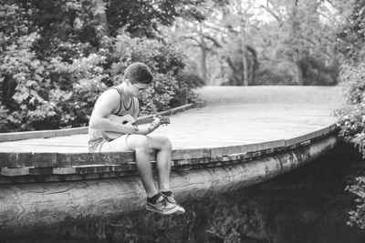 Full length of man playing ukulele on footbridge against trees