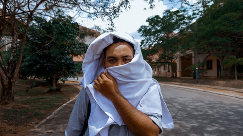 Portrait of man covering face with textile against trees