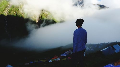 Rear view of man standing on mountain during foggy weather