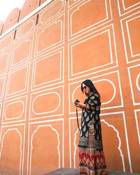 Woman photographing with camera standing against wall