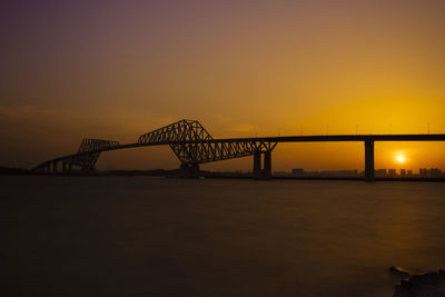 Silhouette bridge over river against sky during sunset