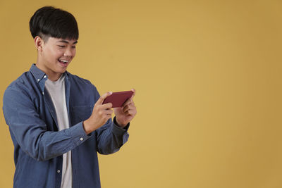 Man holding camera while standing against wall