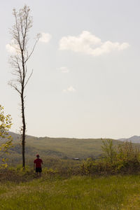 Rear view of woman sitting on field against sky