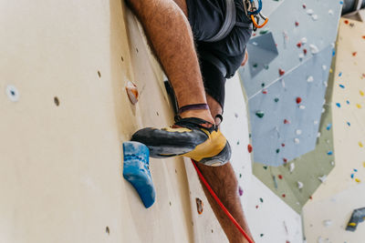 Crop anonymous sportive male alpinist with belay climbing up artificial wall with colorful grips during intense training in light gym