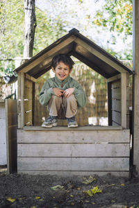 Portrait of happy boy crouching on wooden hut at park