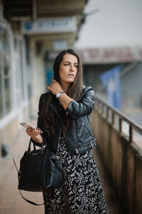 Casual young woman in dress and leather jacket is walking and wa