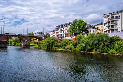 Arch bridge over river by buildings against sky