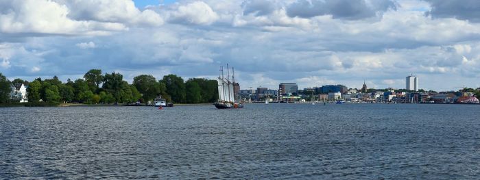 Sailboats in sea by buildings against sky