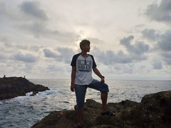 Man standing on rock by sea against sky