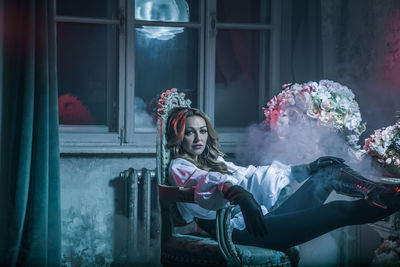 Portrait of woman in costume sitting on chair at home during night